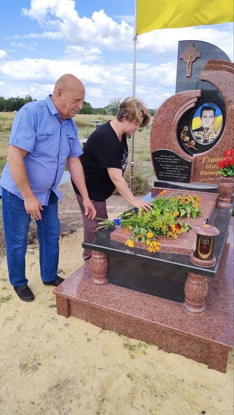 На рисунку зображено двох людей, які прийшли на могилу загиблого героя України. Вони кладуть квіти на його могилу
